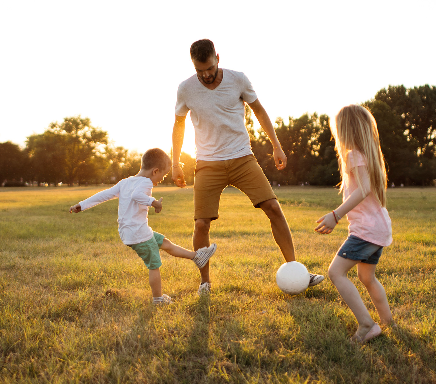 Family playing with soccer ball in a field at sunset